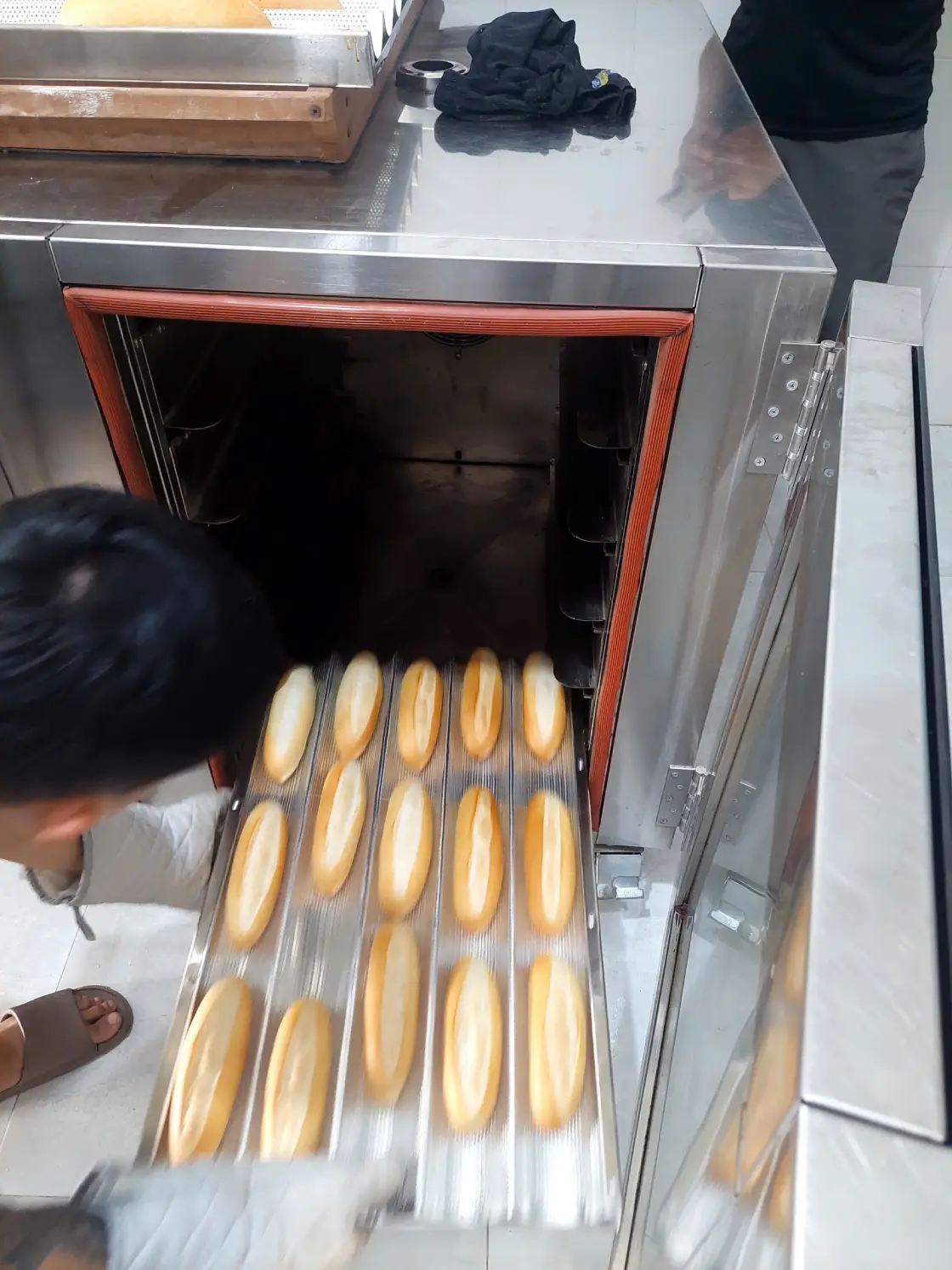 Nhân viên dùng găng cách nhiệt lấy khay bánh mì ra khỏi lò nướng tại cửa hàng Đông Hòa.